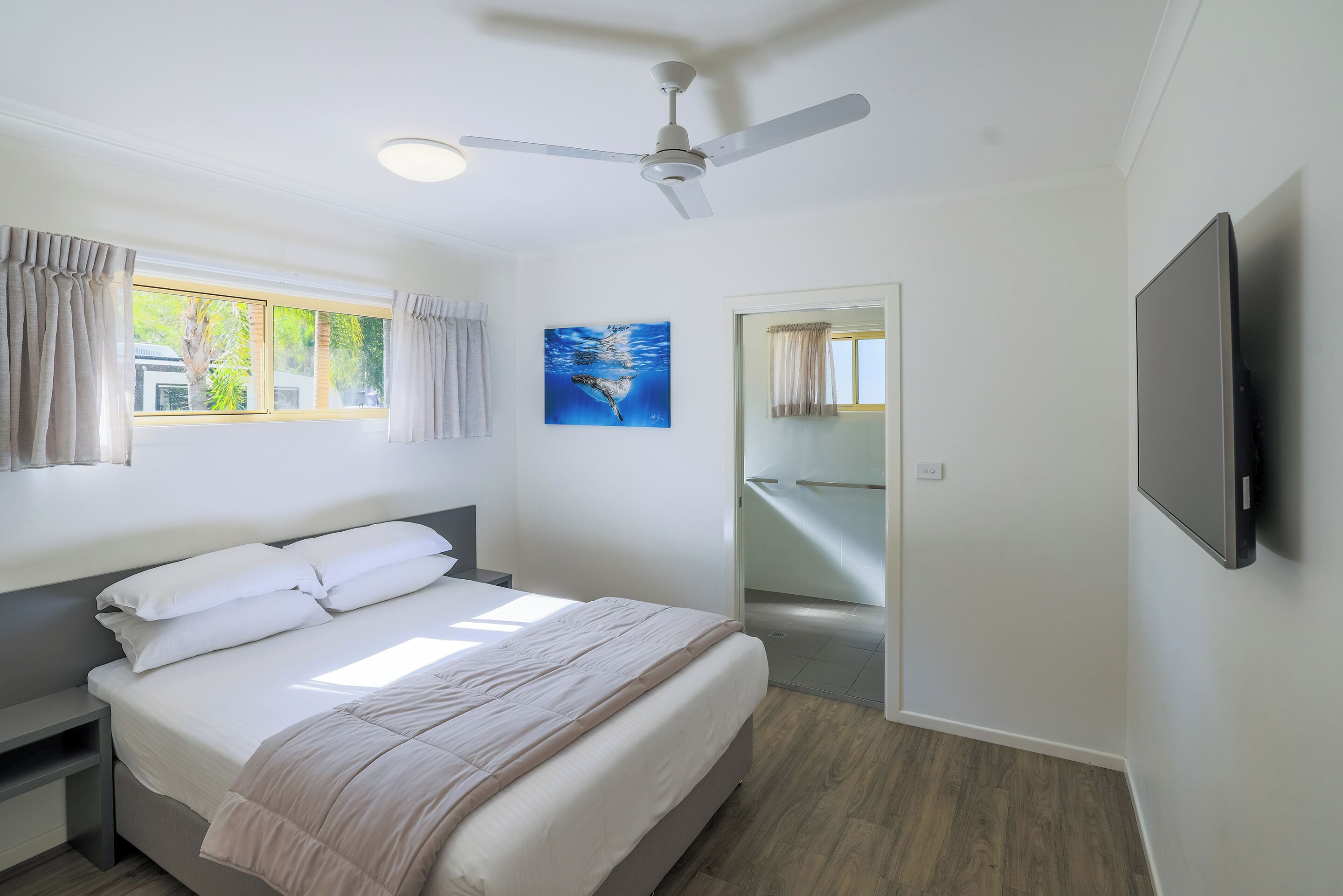 Une chambre à coucher avec un lit, un ventilateur de plafond, une télévision et un tableau au mur.