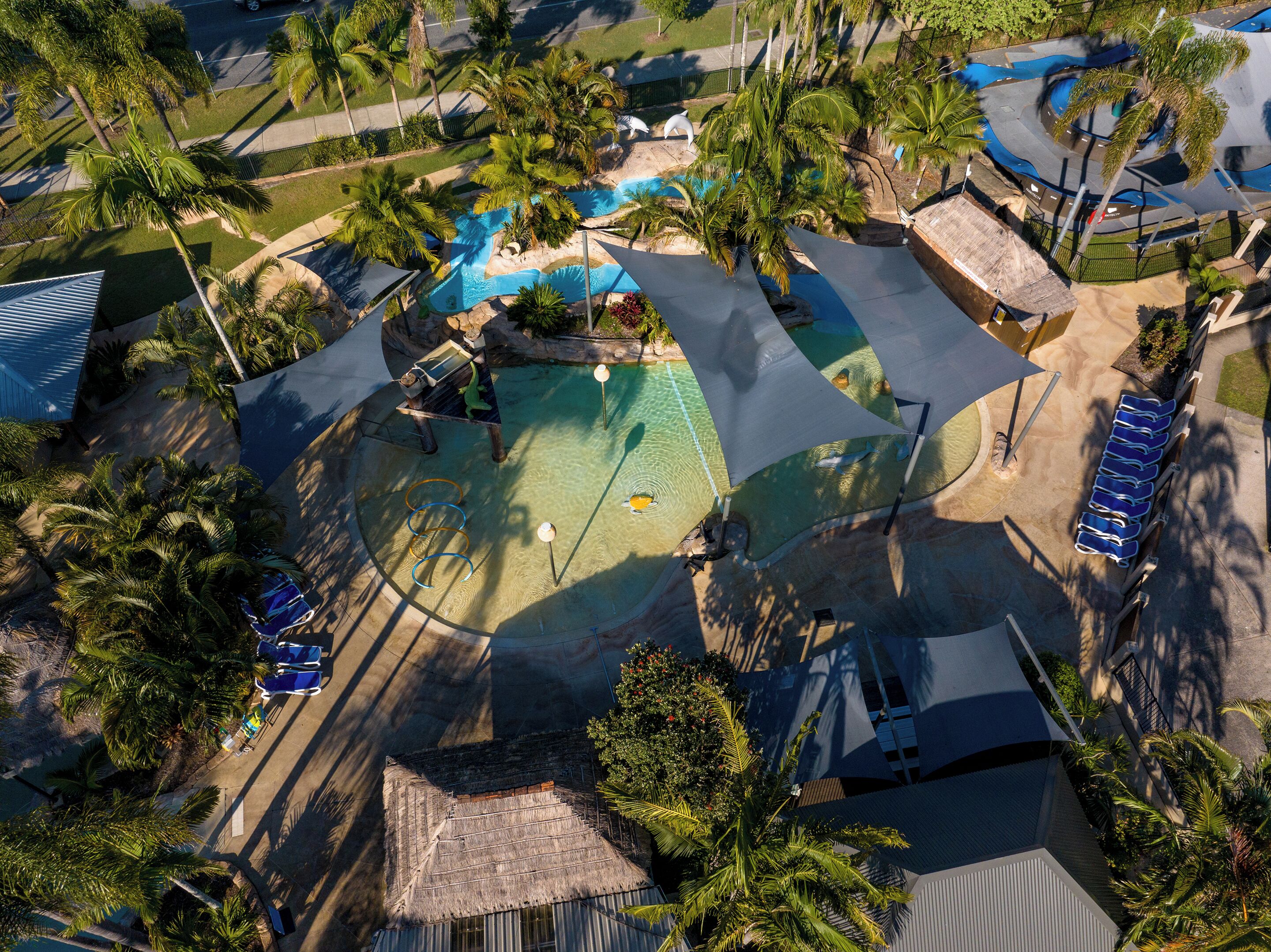 An aerial view of a resort with a swimming pool, palm trees, and lounge chairs.