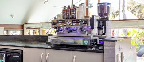 A coffee machine with a digital display, stacked cups, and condiment bottles on a counter.