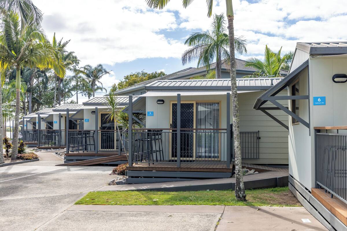 A row of small, single-story cabins with balconies, surrounded by palm trees.