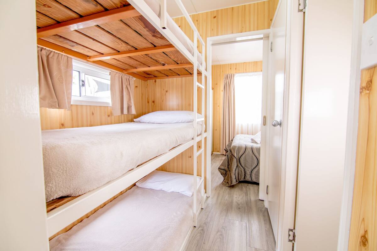 A bunk bed room with a wooden ceiling and a window with curtains.