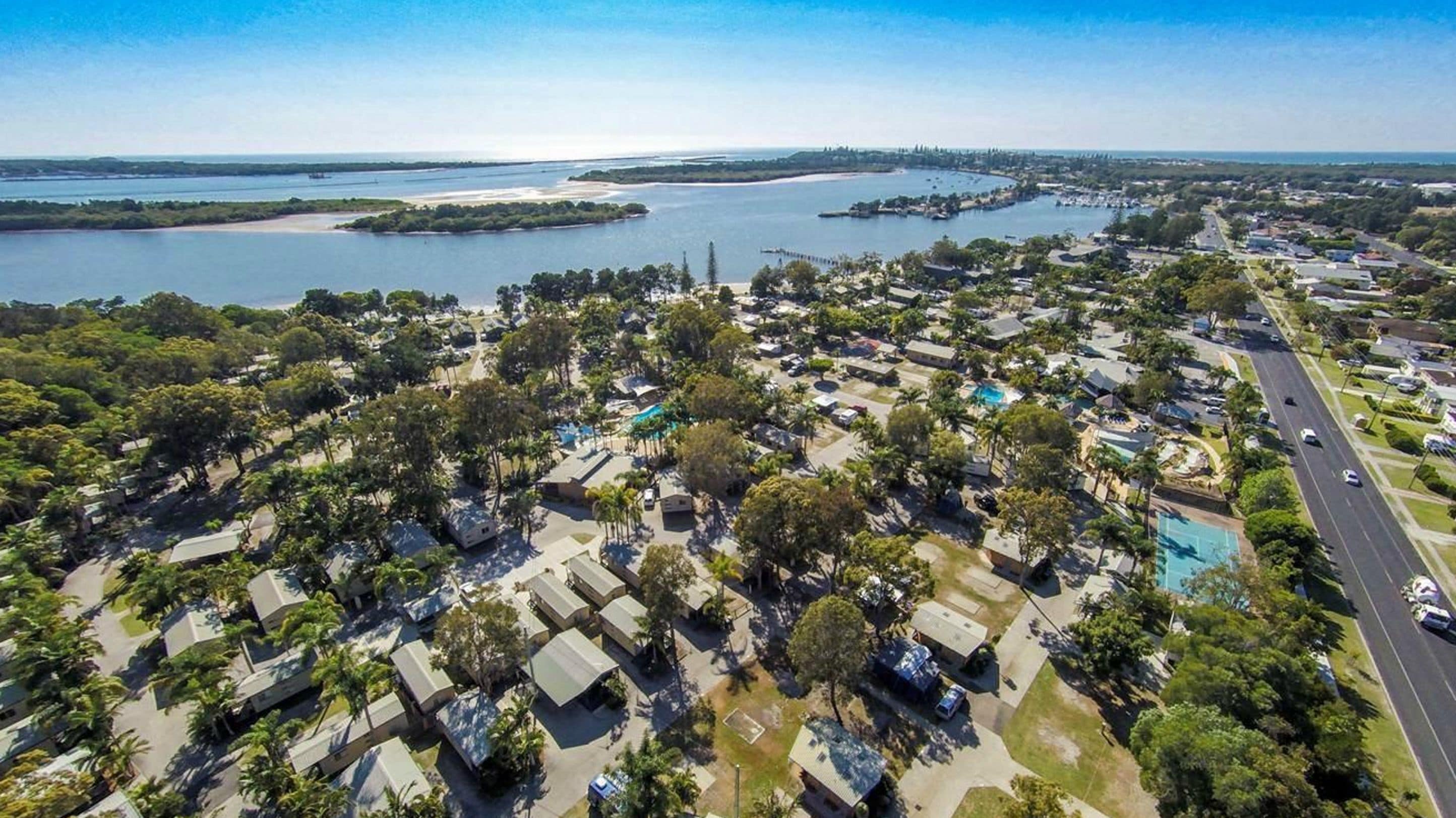 An aerial view of a coastal residential area with houses, a road, and a large body of water.