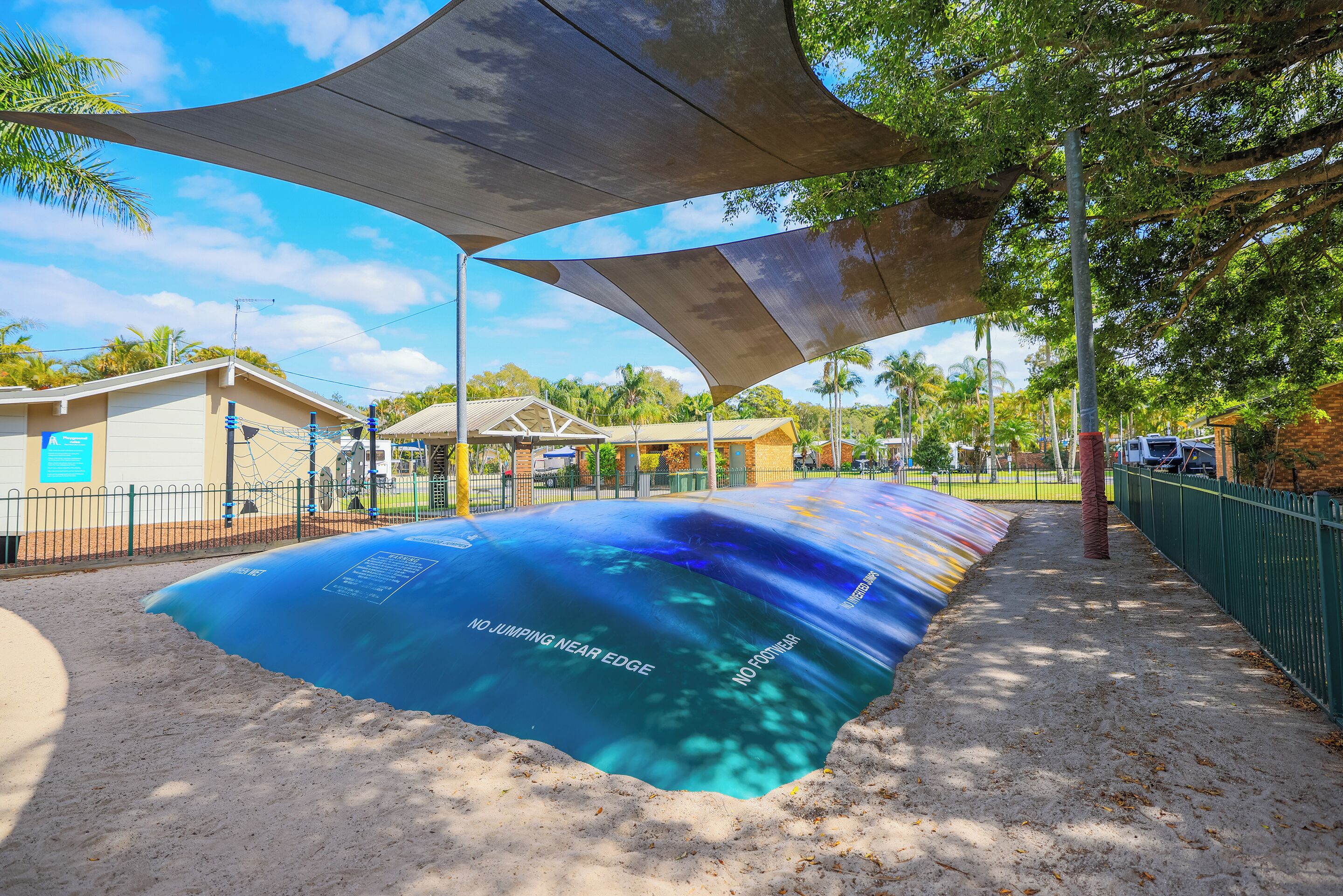 A sandy area with a blue surface, a fence, and trees in the background.