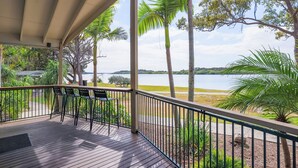 A covered outdoor area with a wooden deck, chairs, and a view of a lake and surrounding greenery. - NRMA Blue Dolphin Yamba Holiday Resort (Yamba)