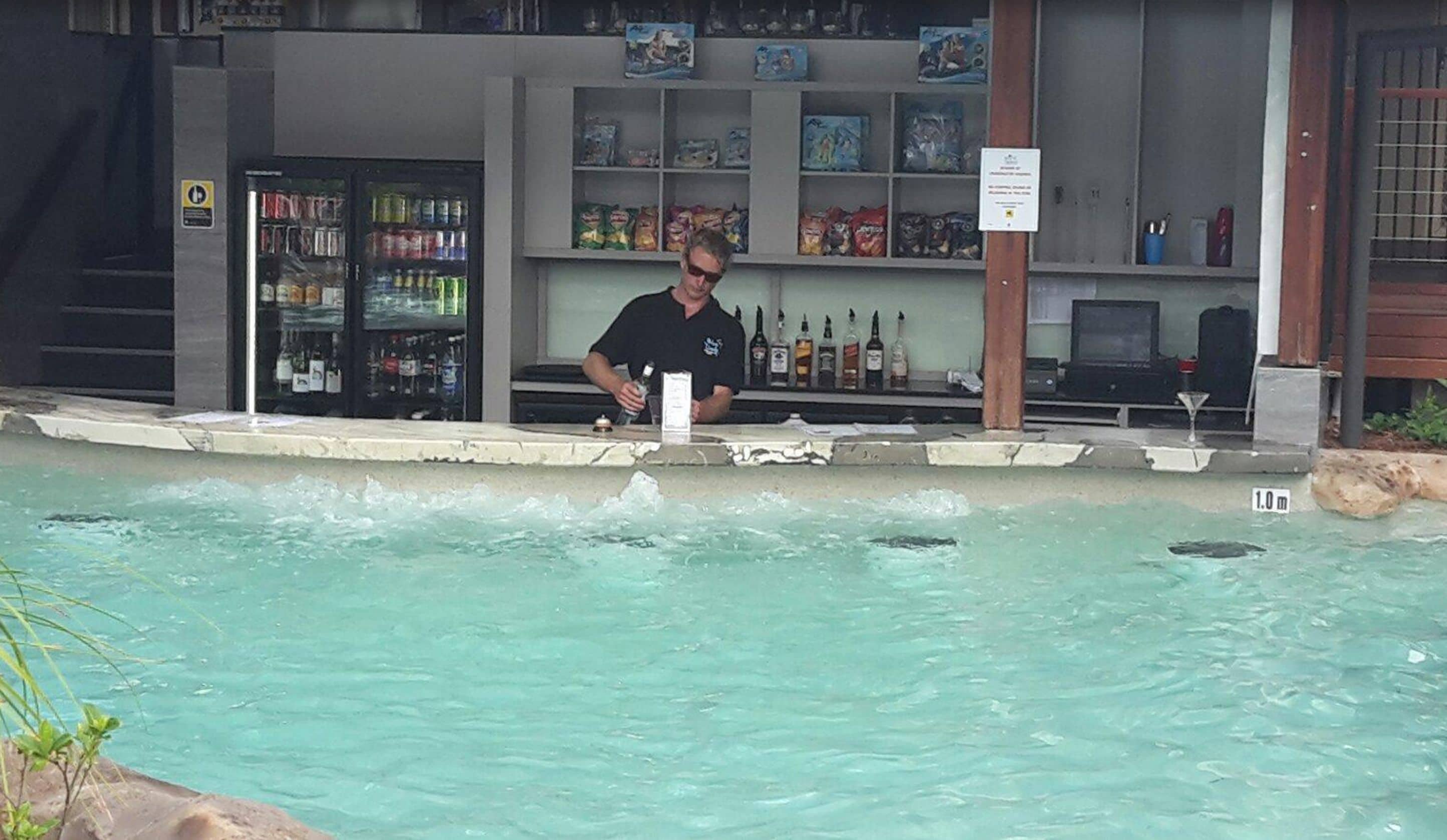 A bar area with a pool, bar counter, and shelves with various bottles.