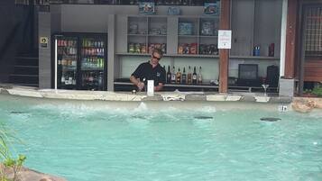 A bar area with a pool, bar counter, and shelves with various bottles.