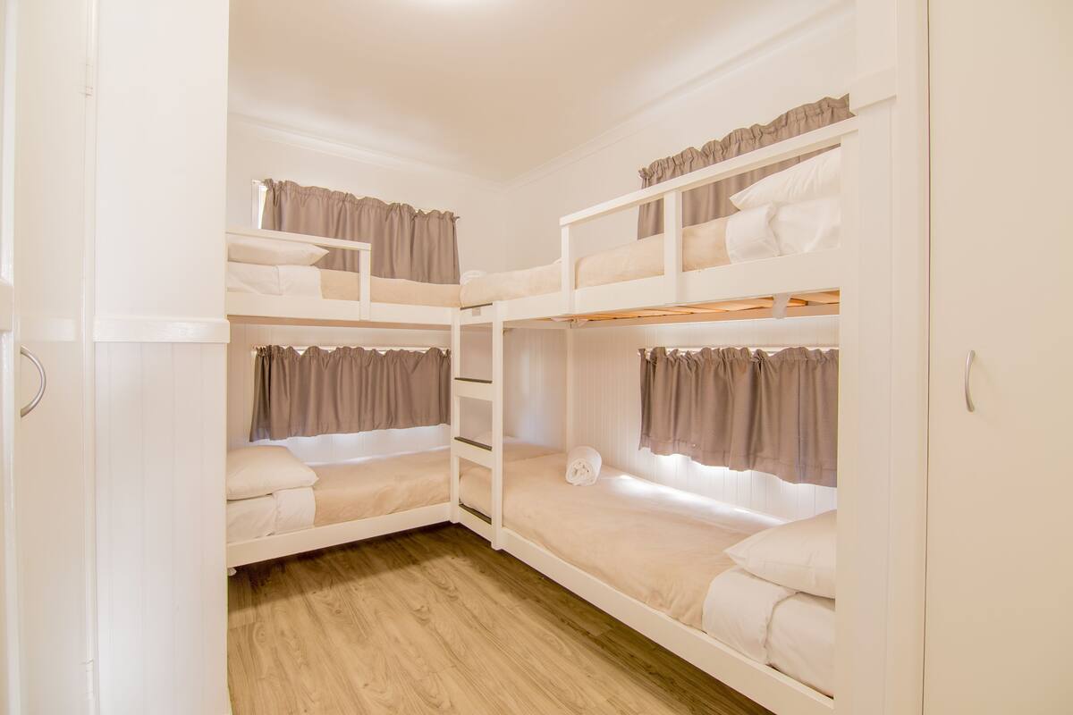 A bunk bed room with white bedding, curtains, and wooden flooring.