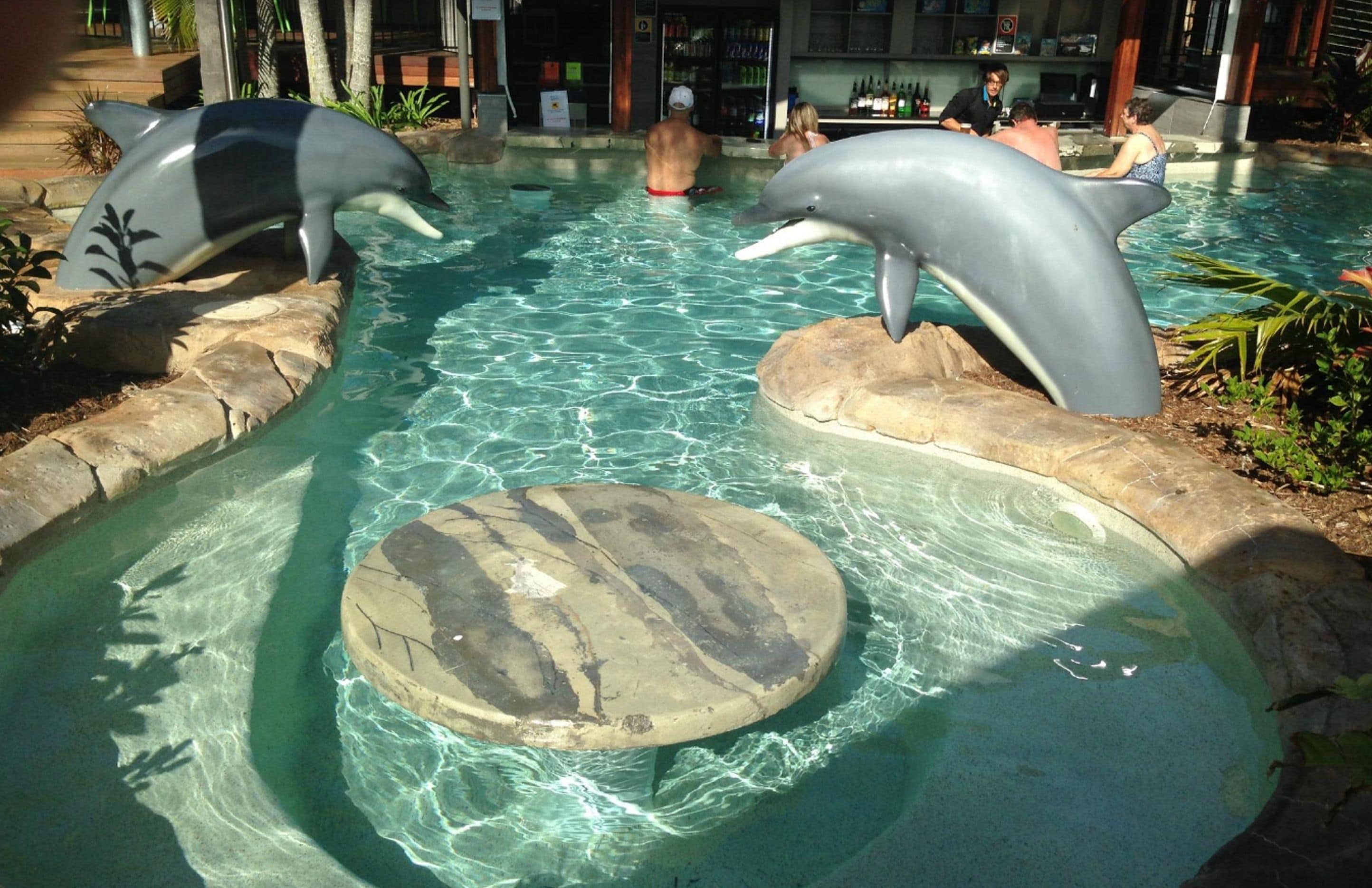 A swimming pool with dolphin sculptures and a central stone platform.