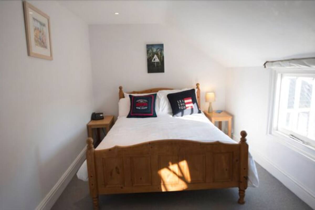 A bedroom with a wooden bed, white bedding, a bedside table with a lamp, and a framed picture on the wall.