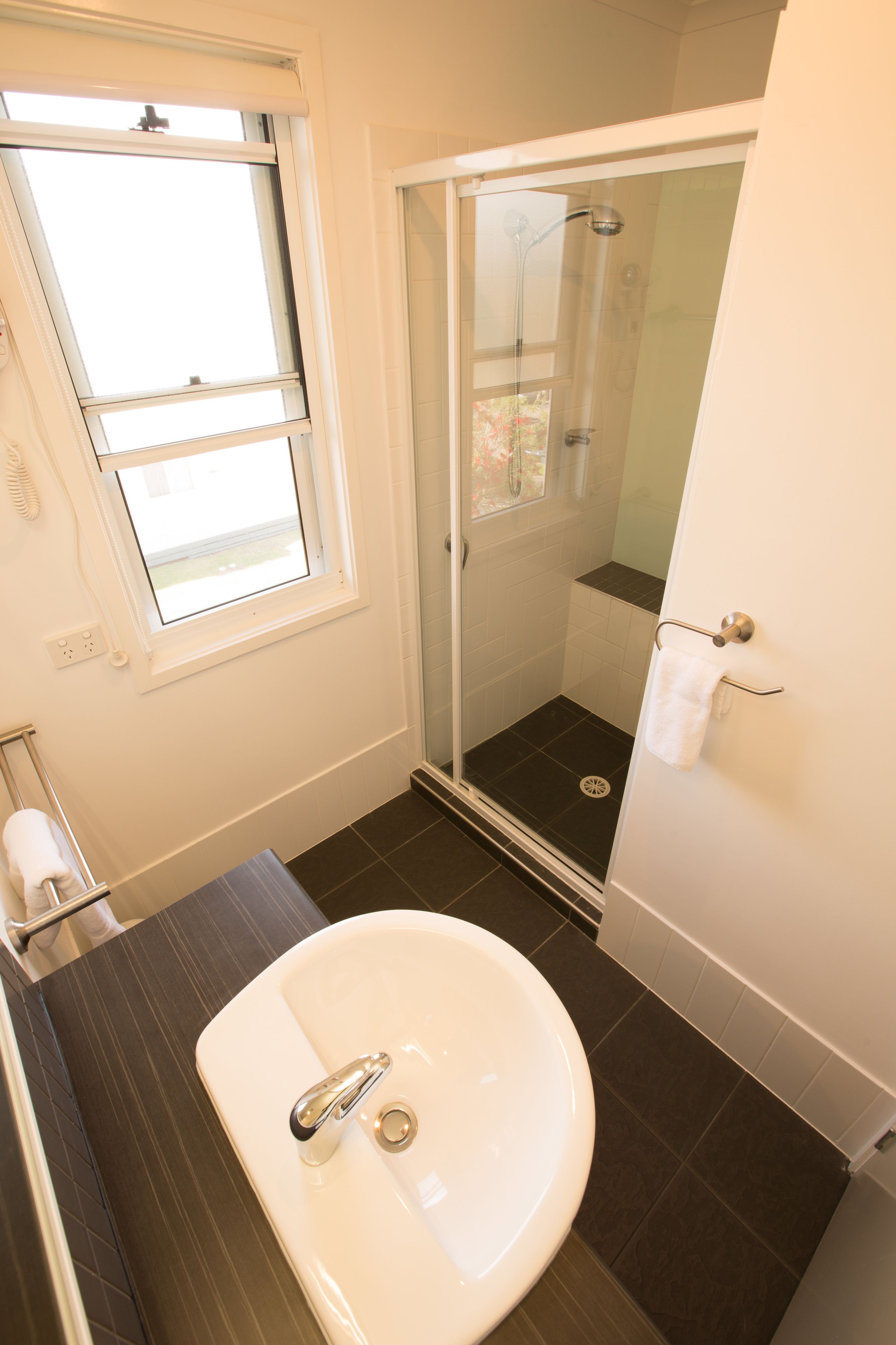 A bathroom with a white sink, a glass shower enclosure, and a window providing natural light.