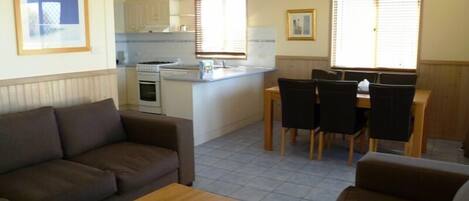 Un espacio habitable compacto con un sofá, una mesa de centro, una zona de comedor con mesa y sillas, y una cocina con estufa y armarios.