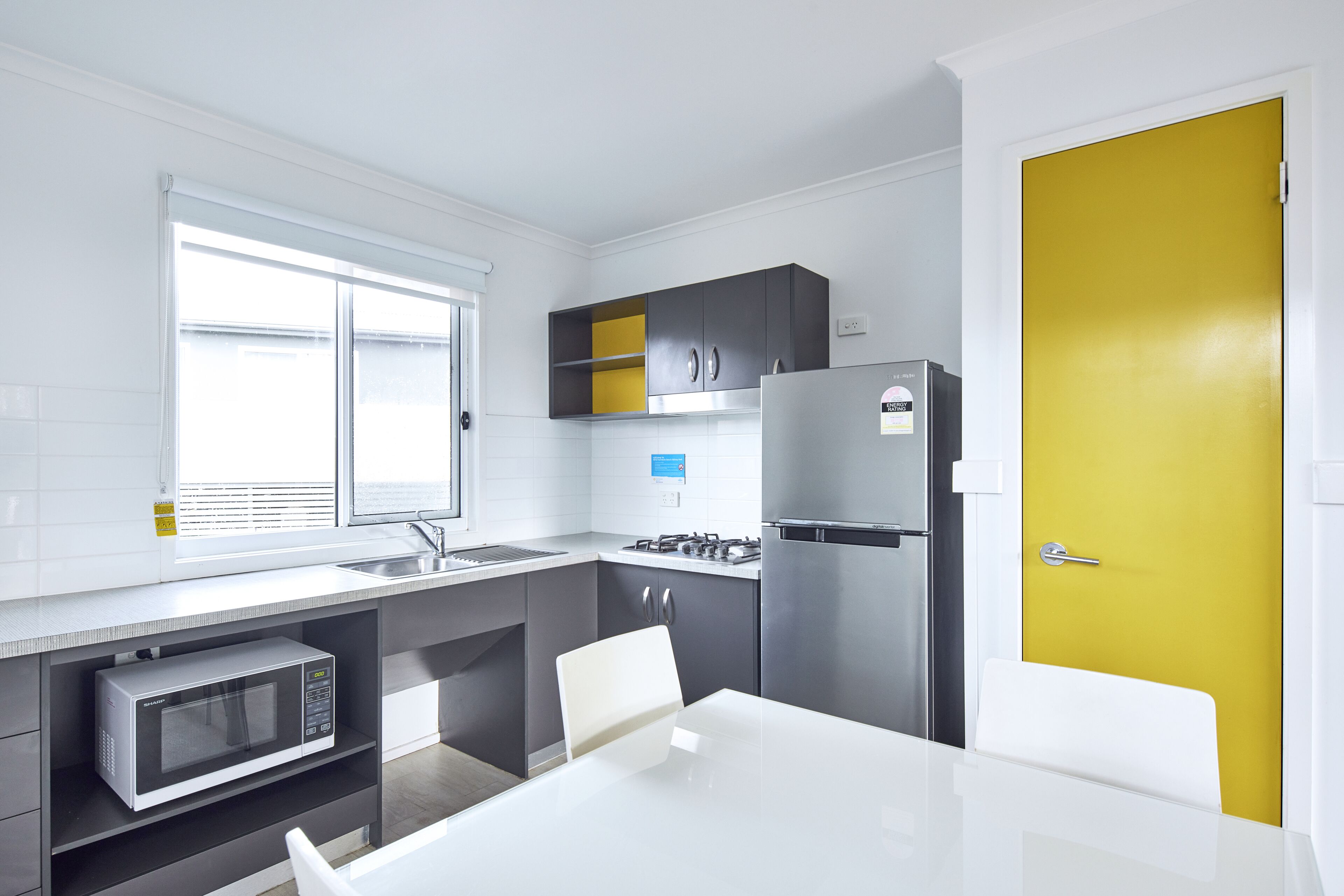 A modern kitchen with a white countertop, stainless steel appliances, and a yellow door.