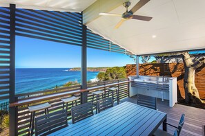 An outdoor deck with a view of the ocean, a ceiling fan, and a built-in kitchen area. - NRMA Merimbula Beach Holiday Resort (Merimbula)