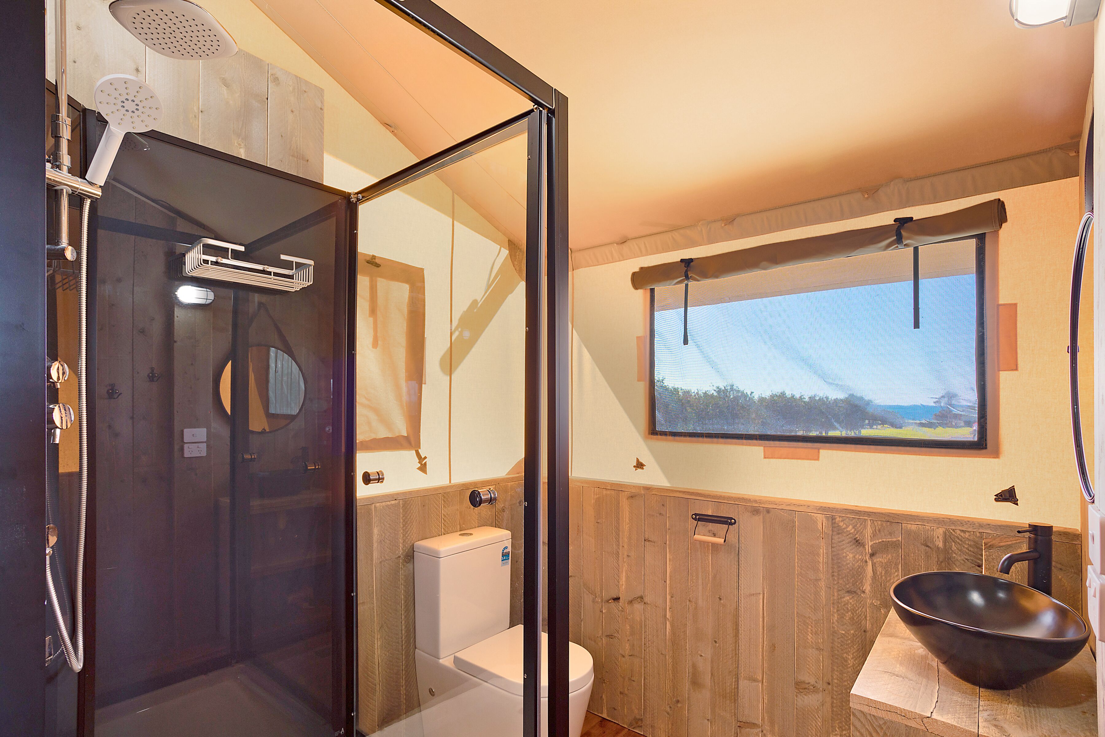A bathroom with a glass-enclosed shower, a toilet, and a large window.