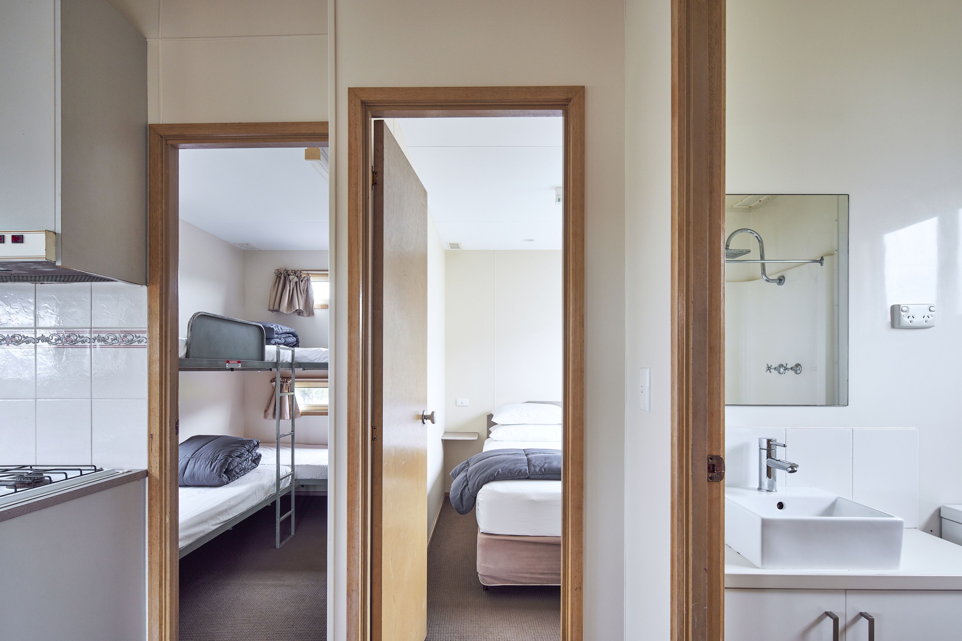 A compact hotel room with a kitchenette, a single bed, a small bathroom with a mirror, and a view into the corridor.
