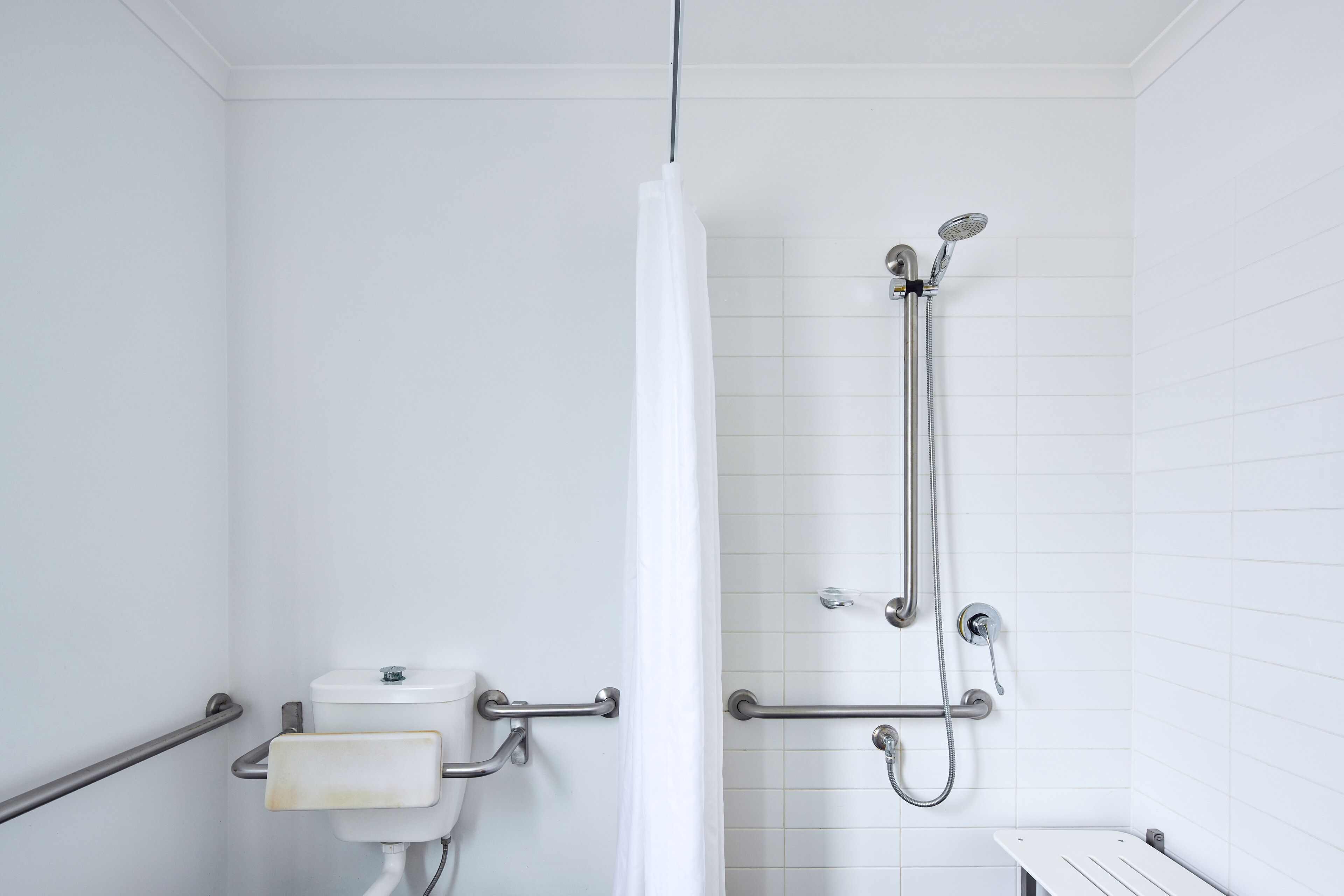 A bathroom with a shower, toilet, and grab bars.