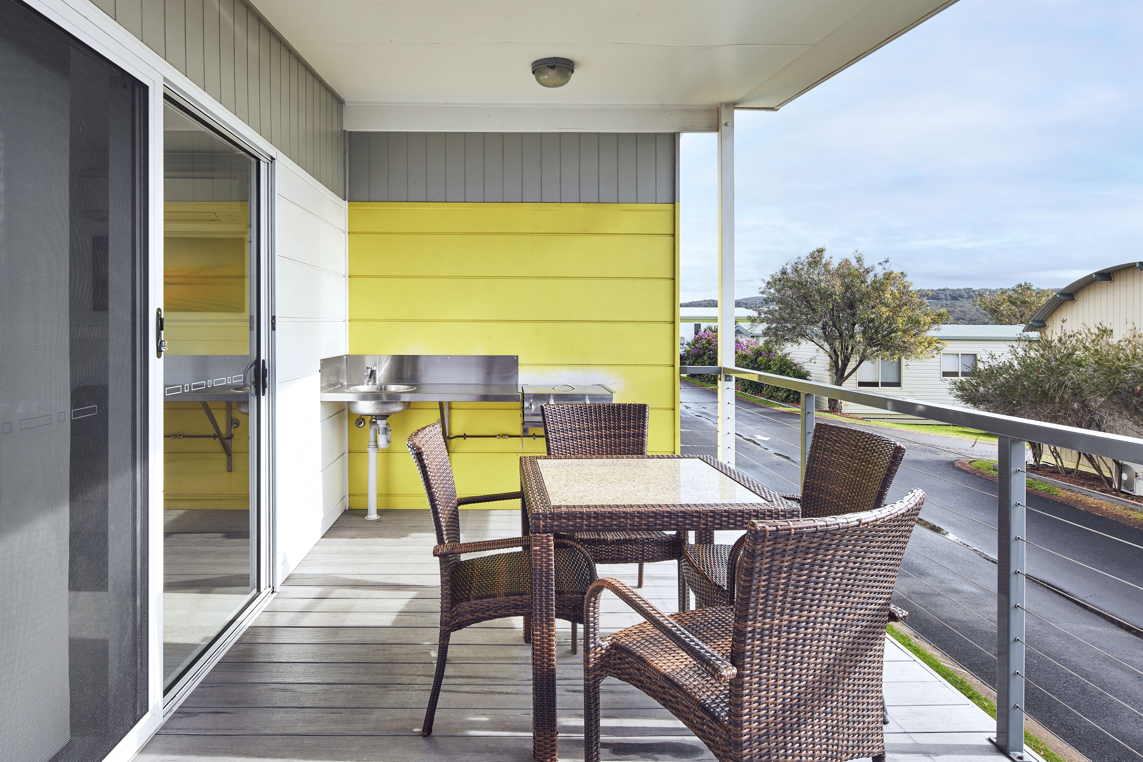 A balcony with wicker furniture, a grill, and a view of the street.