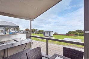 Un patio exterior con barra de acero inoxidable, mobiliario de mimbre y vista a una zona residencial con una casa pequeña y un césped.