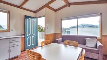 A room with a wooden dining table, chairs, a sofa, and a kitchen area with cabinets and a door.