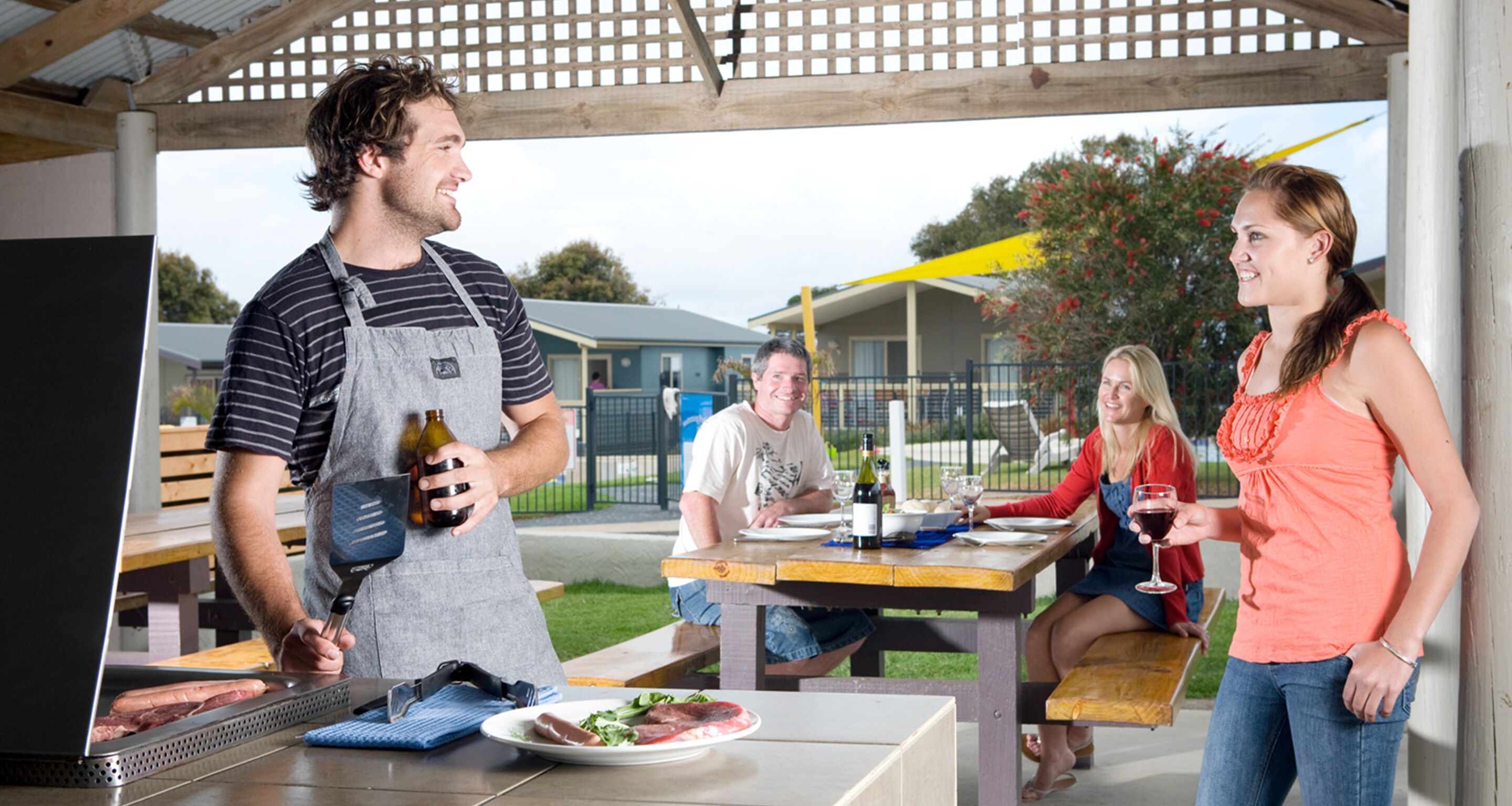 Un espacio de comedor al aire libre techado, con una parrilla, una mesa con comida y un banco.