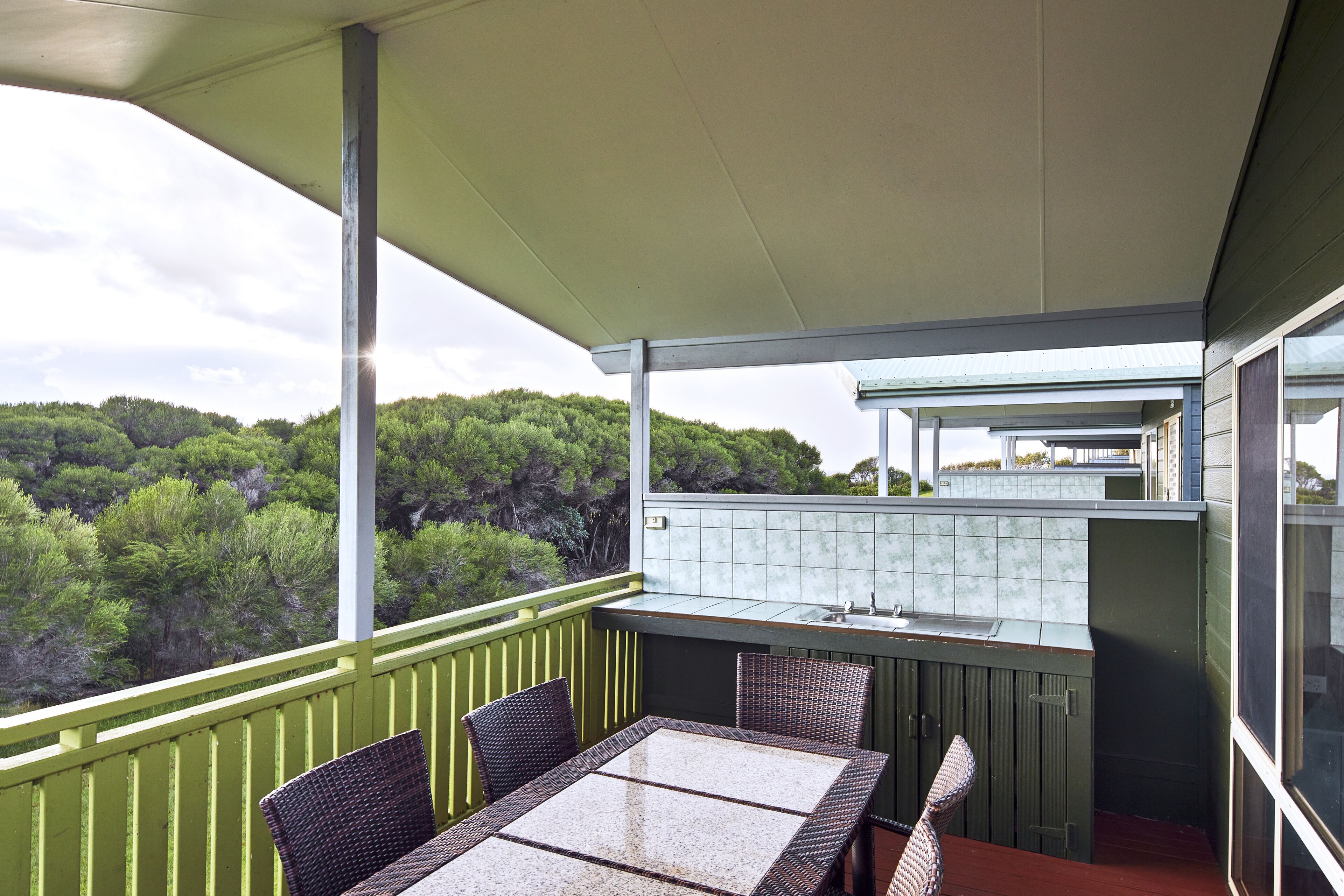 Een balkon met een tafel, stoelen, een wastafel en uitzicht op een bebost gebied.