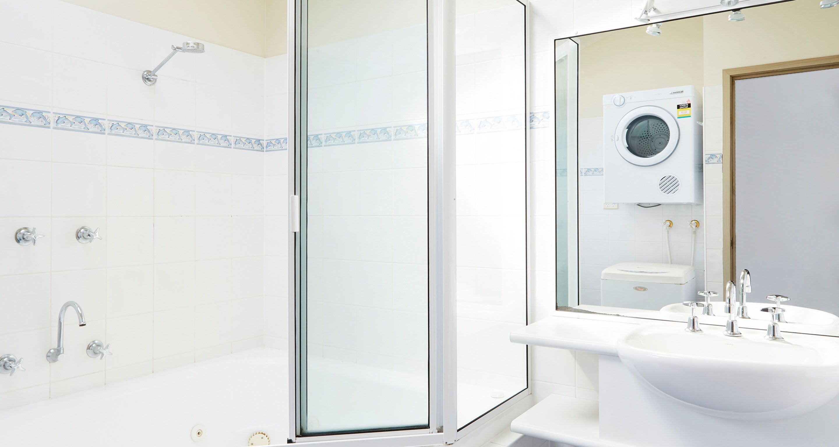 Un baño moderno con cabina de ducha de vidrio, un lavamanos blanco con múltiples grifos y una lavadora empotrada.