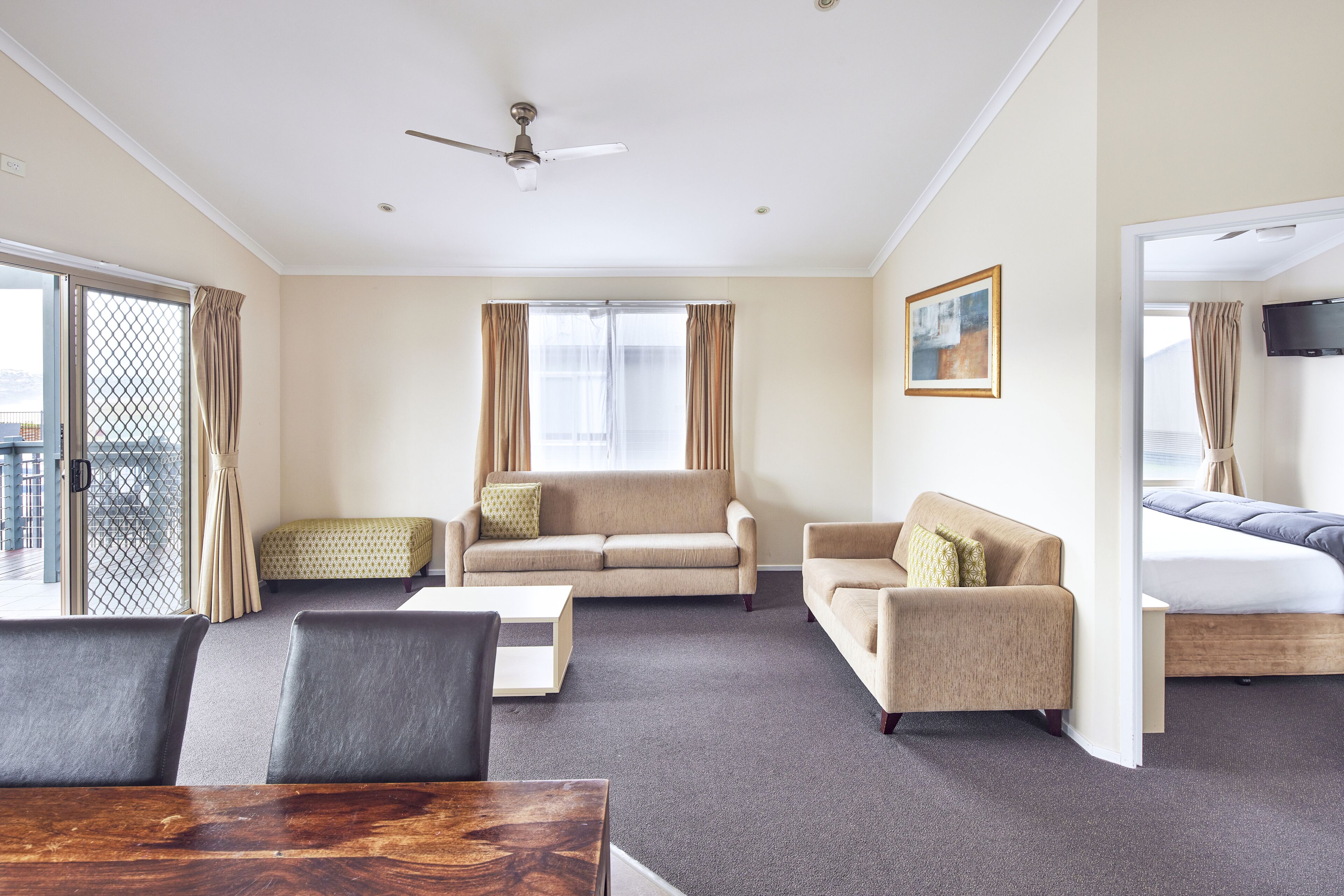 A hotel room with a sofa, two armchairs, a coffee table, a TV, and a bed.
