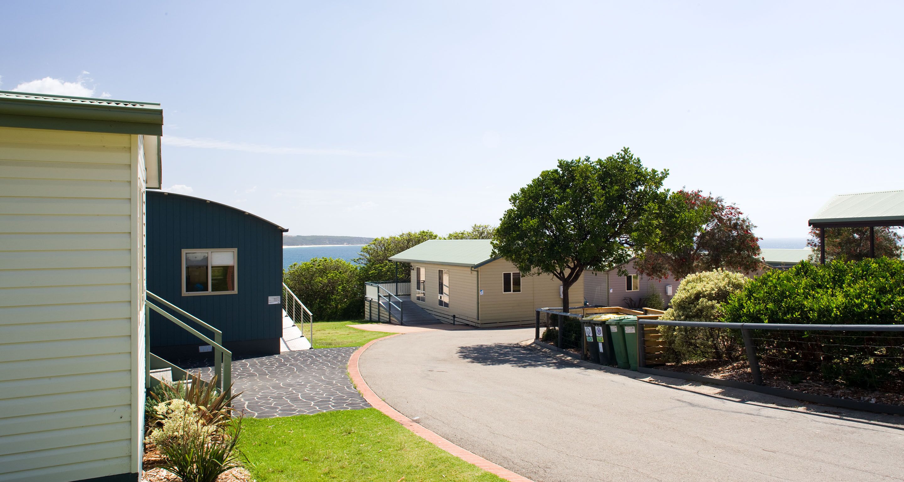 A residential area with a curved driveway leading to a house with a green roof, a tree, and a view of the water.