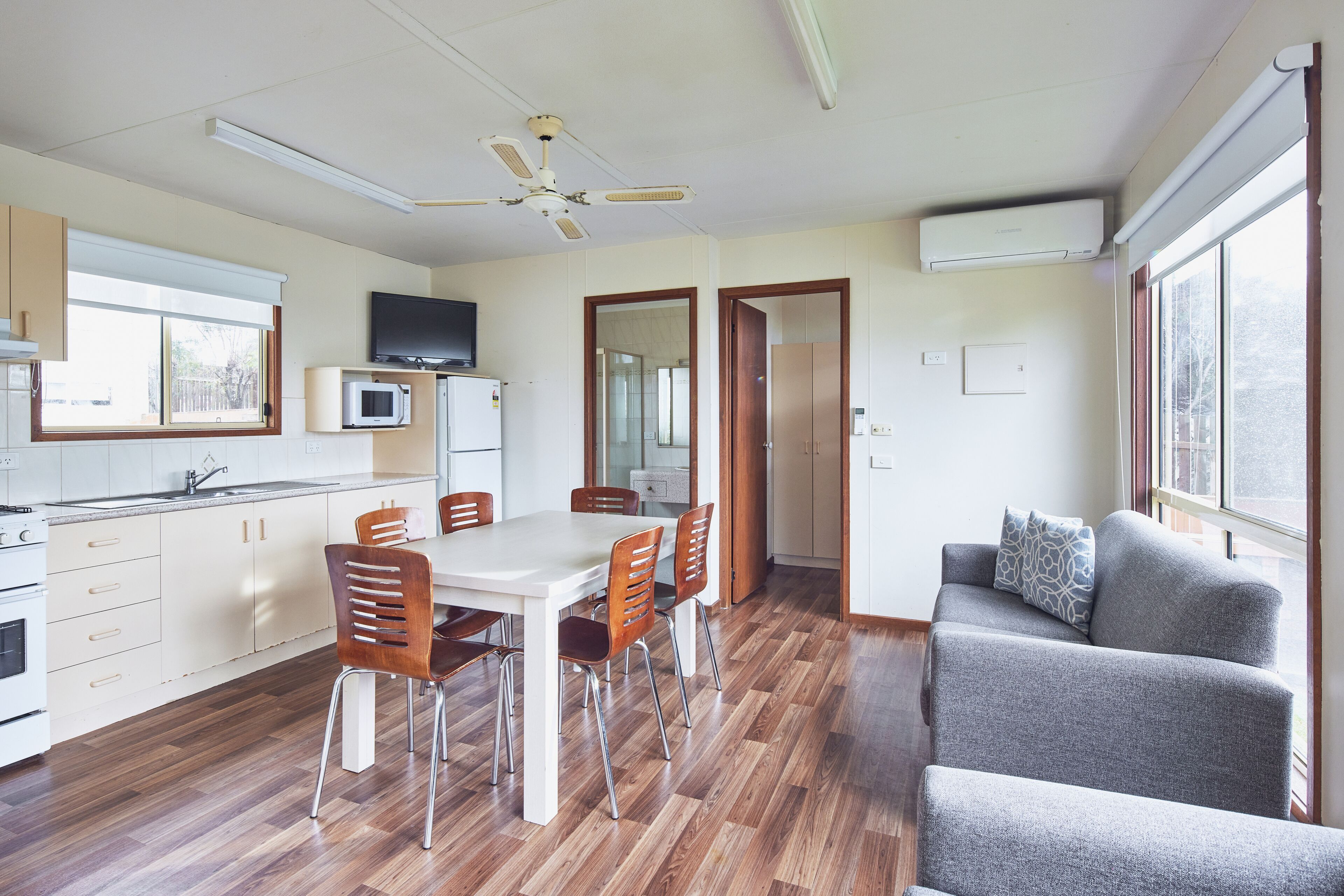 A modern kitchen with a dining area, a grey sofa, and a ceiling fan.