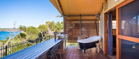 A wooden deck with a table and chairs, a hot tub, and a view of the ocean.