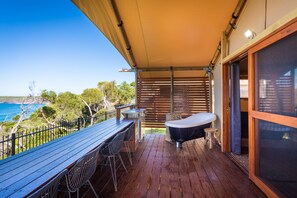 Una terraza de madera con mesa y sillas, un jacuzzi y vista al océano.