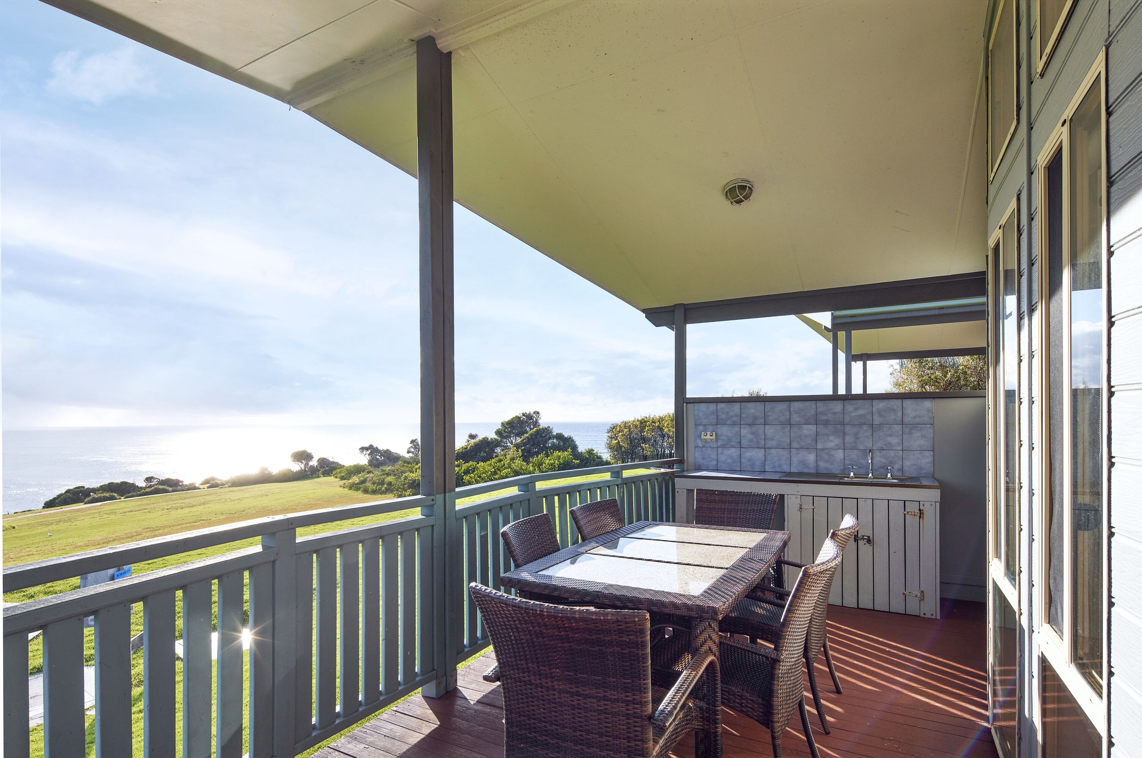 A covered outdoor area with a table and chairs, a built-in sink, and a view of the ocean.