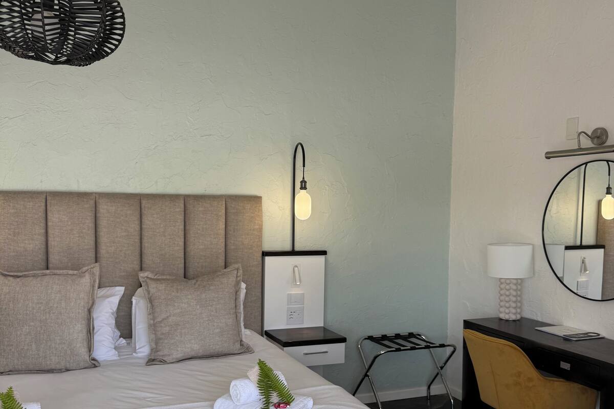 A hotel room with a bed, bedside table, lamp, desk, chair, and a hanging light fixture.