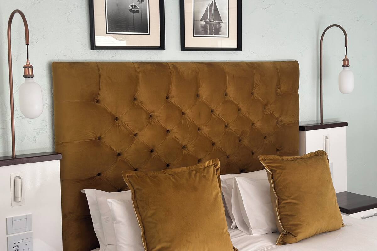 A bed with a tufted headboard, two framed pictures on the wall, and two bedside lamps.