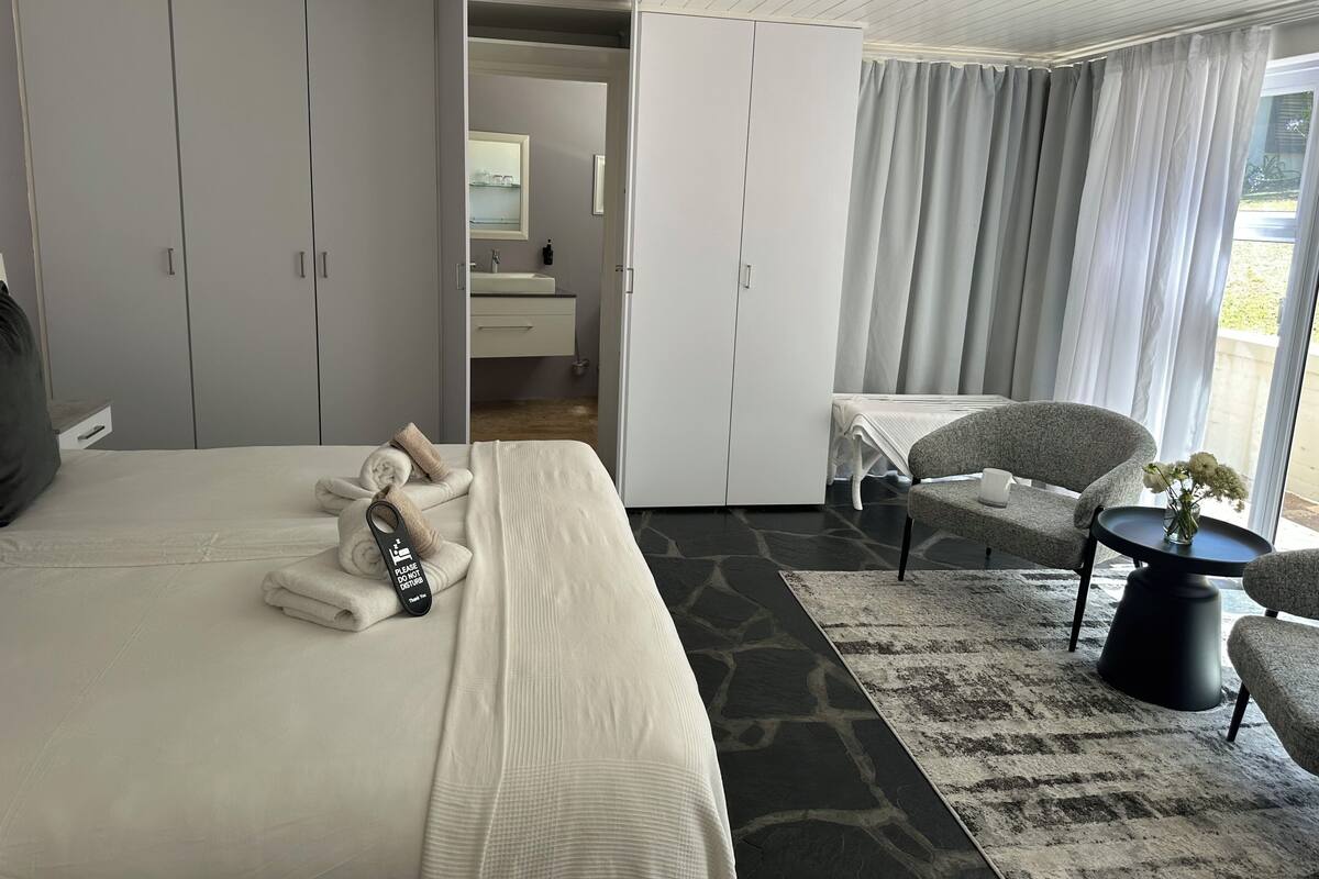 A hotel room with a bed, a chair, a small table, a mirror, a bathroom, and a view of the outdoors.