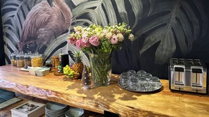 A wooden table with a floral arrangement, jars of condiments, a pineapple, and a toaster. - Southern Cross Guest House (Cape Town)