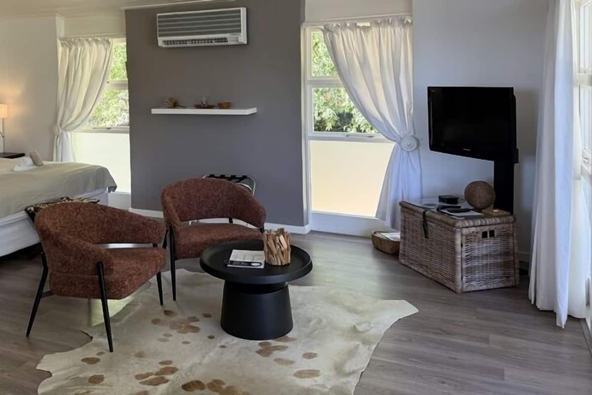 A bedroom with a bed, two chairs, a coffee table, a TV, and a window with curtains.