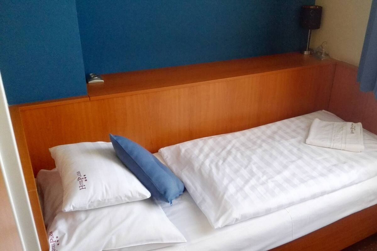 Un lit simple avec une literie blanche et un oreiller bleu, une tête de lit en bois et un mur bleu.