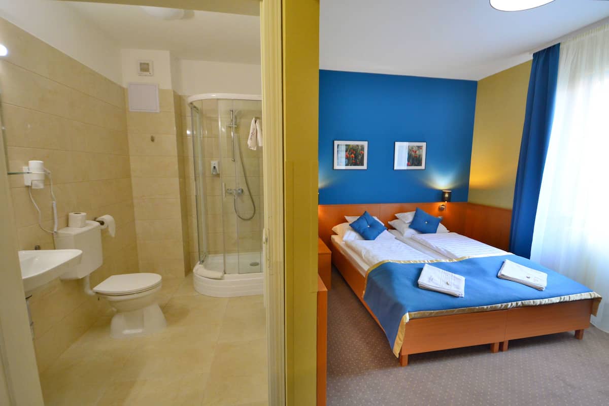 Une chambre d’hôtel équipée d’une douche, de toilettes, d’un lavabo et d’un lit avec une literie et des oreillers bleus.