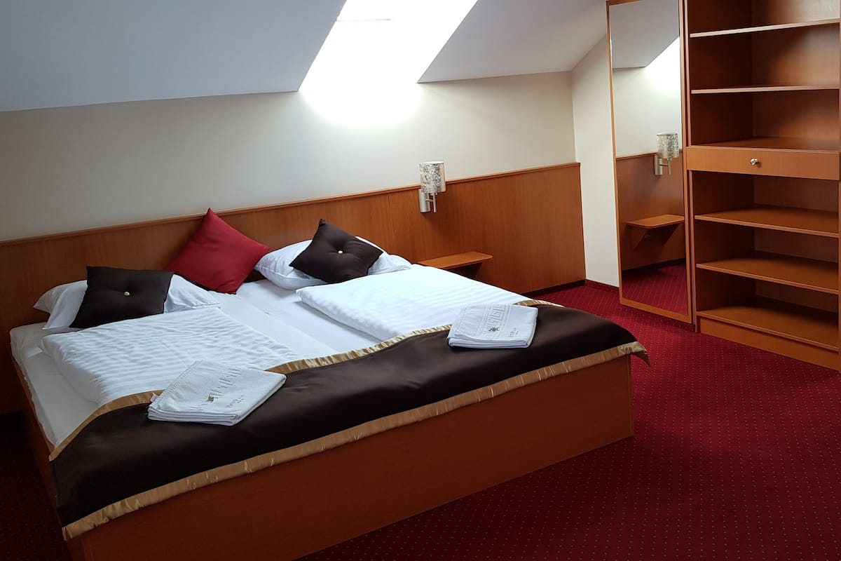 Une chambre d’hôtel avec un lit, une moquette rouge, une armoire en bois et un canapé gris.