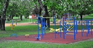 Children can play on the climbing structures and swings in this playground area surrounded by trees and a low fence.