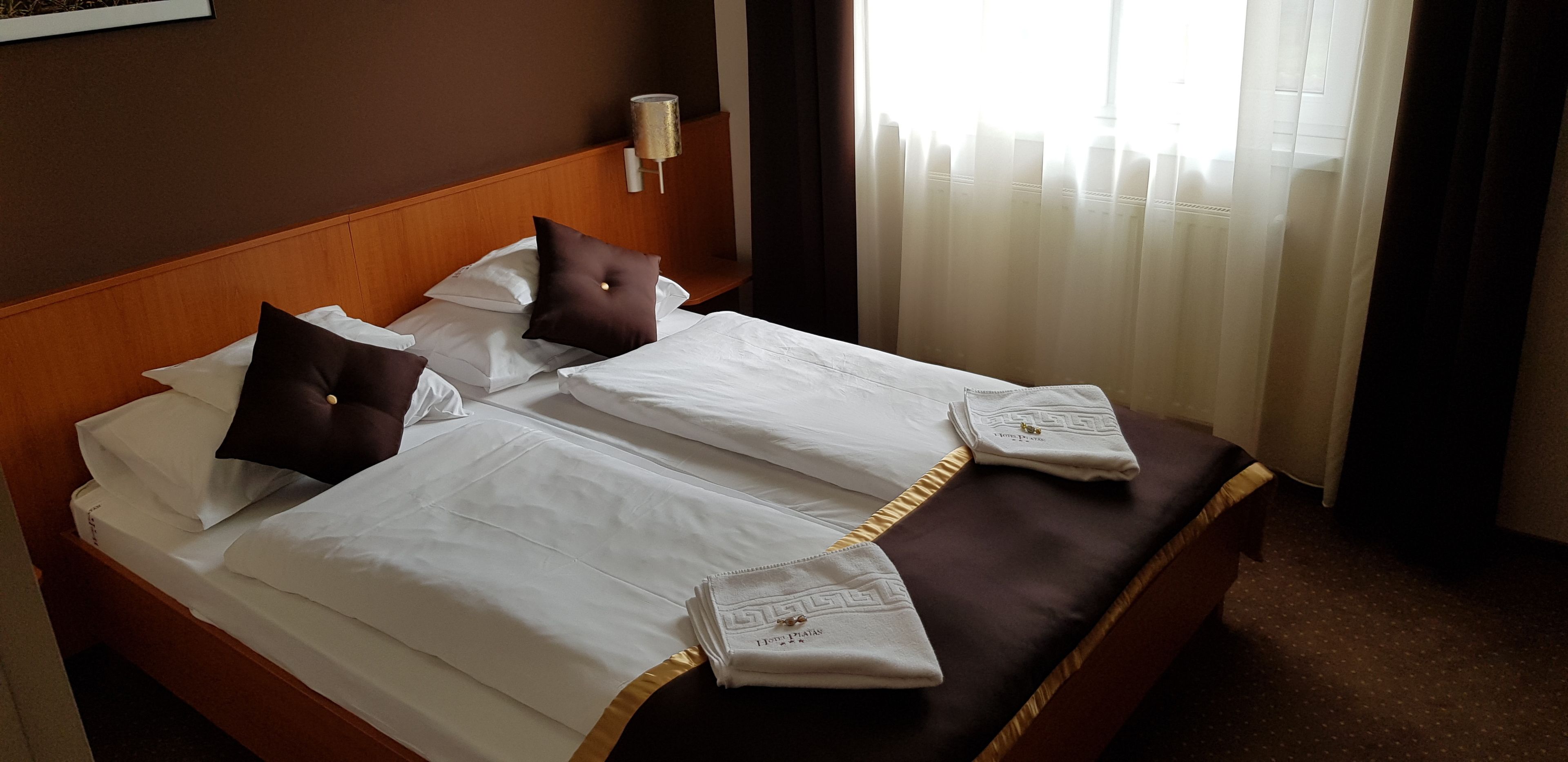 Una cama bien hecha con sábanas blancas y almohadas marrones, un cabecero de madera y una mesita de noche con una lámpara.