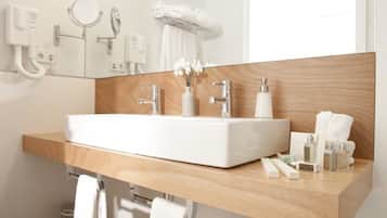 Un baño moderno con un lavamanos grande de color blanco, encimera de madera y un espejo encima. Hay toallas colgadas en un perchero y un pequeño cubo de basura.