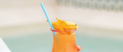 A person holding a cocktail glass with a blue straw and a tropical garnish, near a pool.