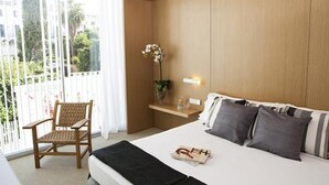 Habitación de hotel con cama, una silla, una mesita y ventana con vistas a zonas verdes.