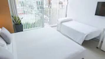 Ein Hotelzimmer mit einem großen Bett, einem an der Wand montierten Fernseher und einem Balkon mit Blick auf die Stadt.