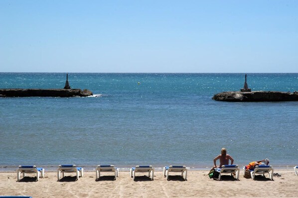 Una playa con filas de tumbonas y dos rompeolas rocosas en el agua.