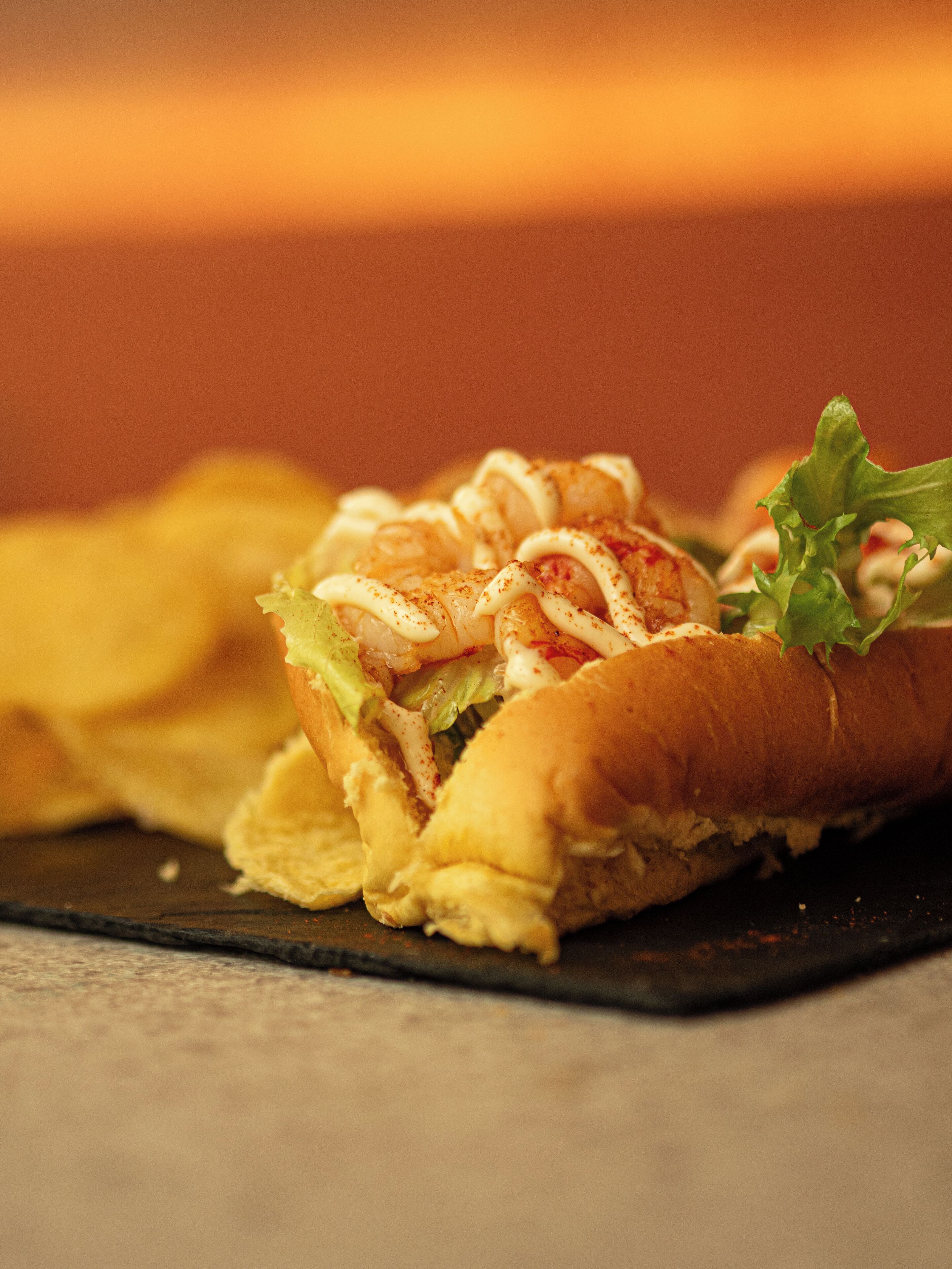 Un sándwich sobre un plato oscuro, con el fondo desenfocado.