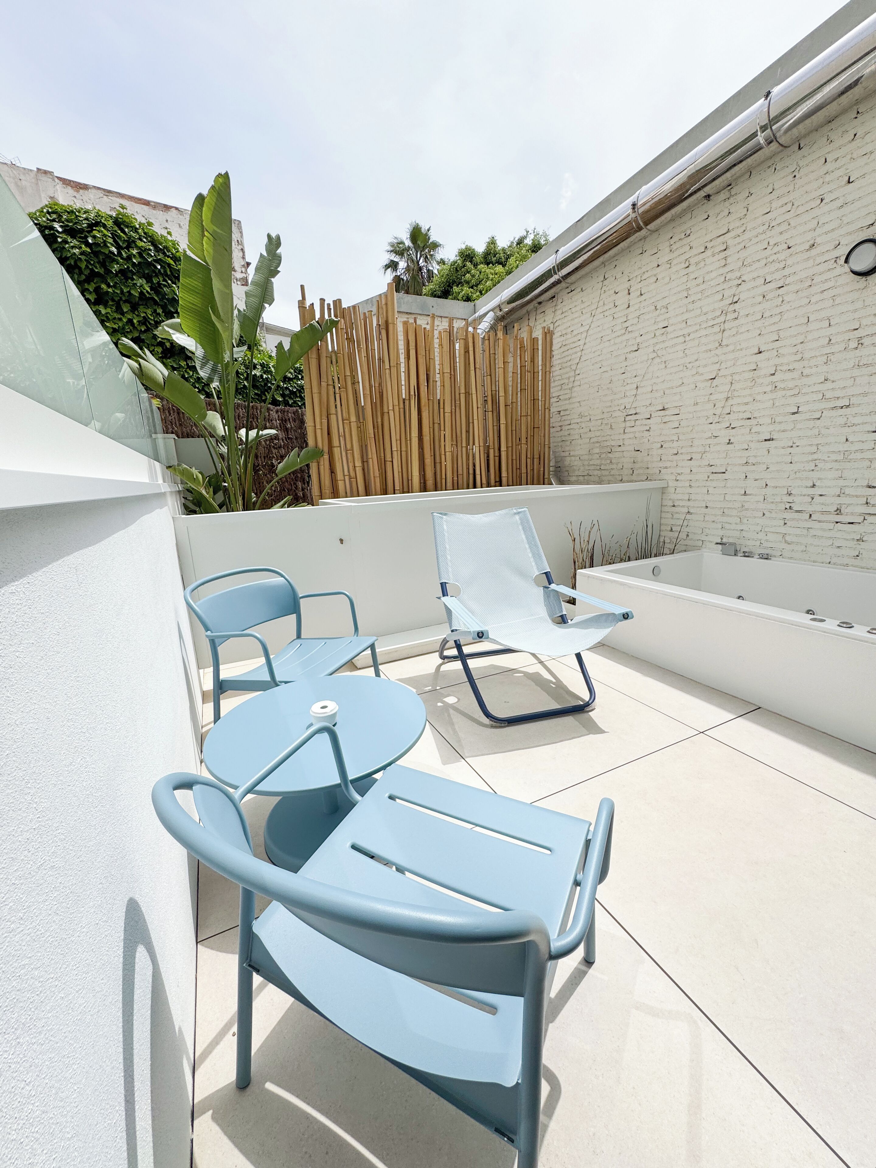 Un patio con sillas azules y una mesa, una bañera blanca y una cerca de bambú.