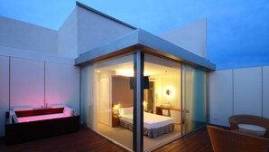 Una habitación de hotel moderna con balcón de cristal, una cama, un escritorio y una silla.